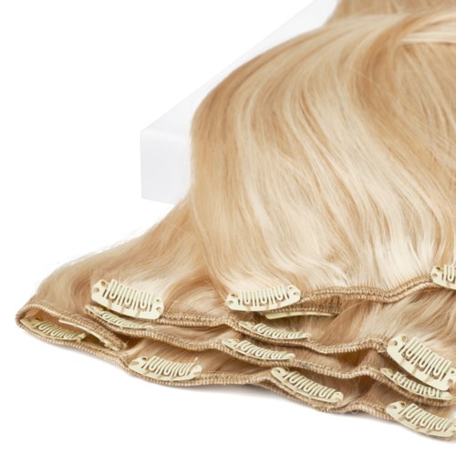 A blonde wig with hair clips is placed on a white surface next to a white box.