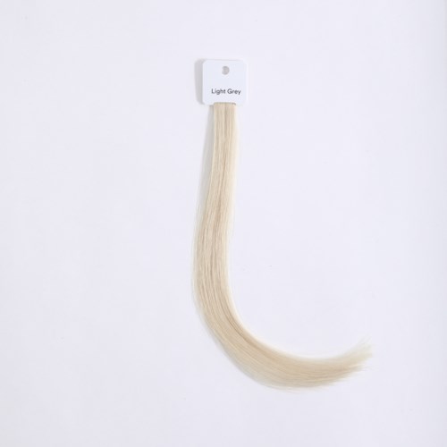 A light grey hair extension hangs from a white card on a white background.