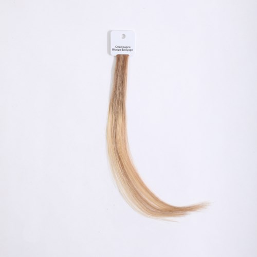 Hårförlängning märkt 'Champagne Blonde Balayage' hänger från en krok på en vit vägg.