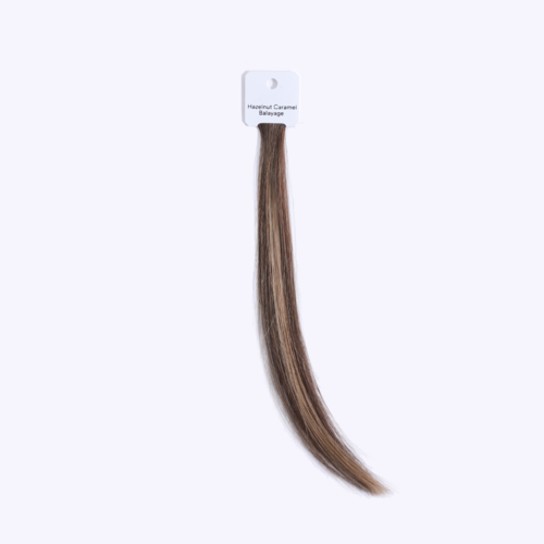 En hårförlängning märkt 'Hazelnut Caramel Balayage' hänger från ett vitt kort.