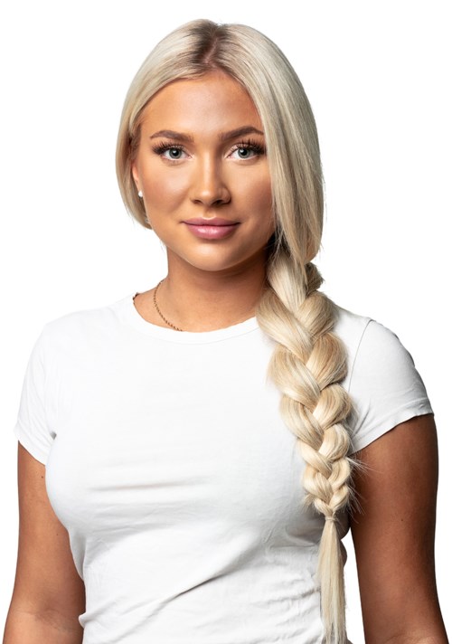 En kvinna med långt blont hår i en fläta, bär en vit t-shirt och tittar mot kameran.