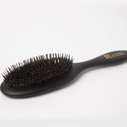Eine schwarze Haarbürste mit vielen Borsten, liegt schräg auf einer weißen Oberfläche.