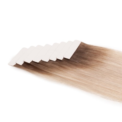 Flere hårextensions er fastgjort til en hvid strimmel, viser en overgang fra mørkere til lysere blondt hår. Meget glat hår.