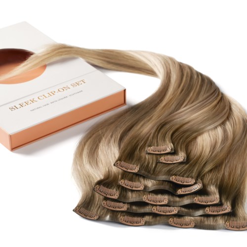 Hårförlängningar i en låda med klipps, staplade, ljusblont. Boxen är märkt "Sleek Clip On Set."