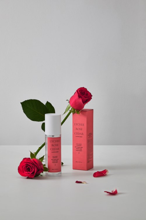 Eine weiße Flasche mit rosa Etikett, rosa Verpackung und zwei rote Rosen auf einer weißen Oberfläche mit Blütenblättern.