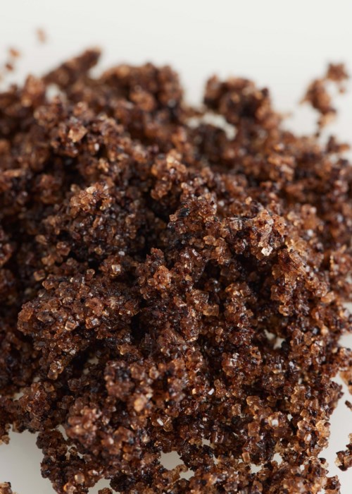 Coffee grounds, dark and coarse, in a small heap on a white surface.