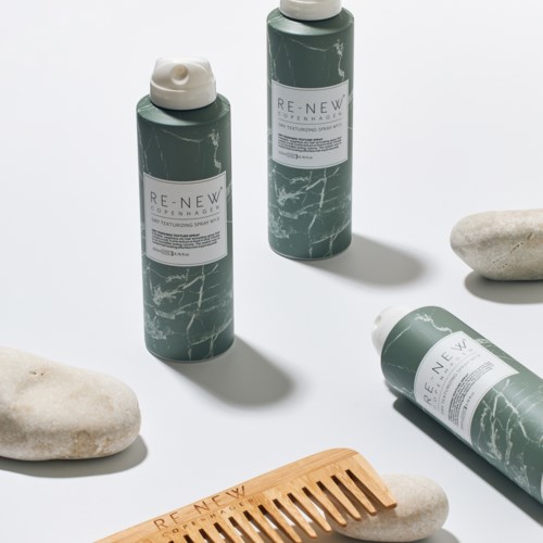 Drie groene flessen met witte doppen, stenen en een houten kam op een witte achtergrond.