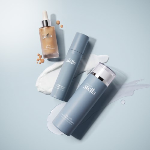 Three skincare products with blue packaging and a dropper bottle, surrounded by cream and liquid on a light background.