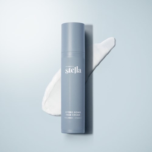 En blå flaska märkt 'Hydro Bomb Face Cream' står upprätt på en slät yta med en klick vit kräm bredvid.