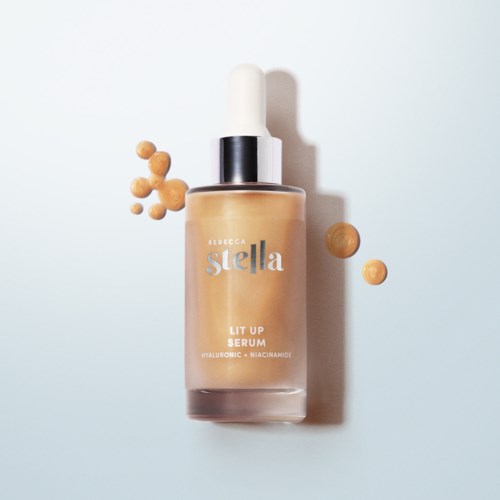 A bottle of serum labeled 'Rebecca Stella' with some beads next to it on a plain background.