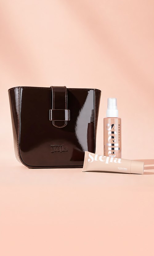 A shiny black toiletry bag with a buckle strap, alongside a pink skincare spray bottle and a tube of cream.