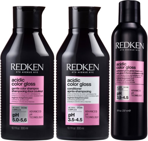 Three black bottles of Redken acidic color gloss hair products stand together. They include shampoo, conditioner, and gloss treatment.