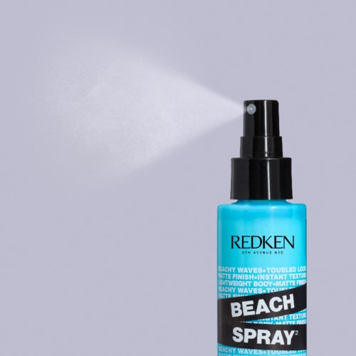 Blue bottle of beach spray with mist coming out, labeled 'Redken'. It is used for hair styling and texture.