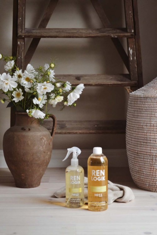 A flower vase with white flowers, cleaning spray bottles, and a basket near a wooden ladder.