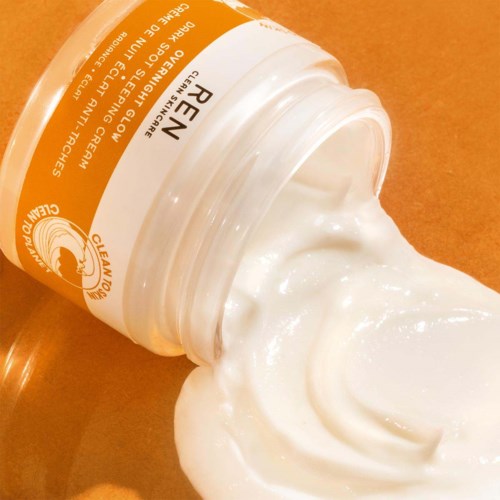 A jar of creamy skincare product with some coming out, placed on a brown surface.