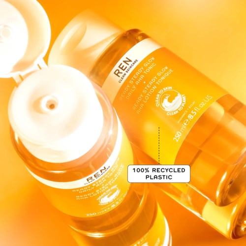Two orange bottles of skincare product, labeled 'Crem', with a white cap and a clear label showing recycled plastic.