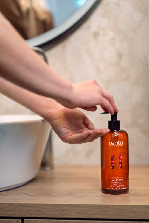 Hands press a pump on an orange bottle labeled 'Rento' on a bathroom counter.