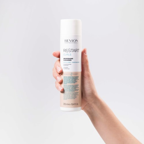 A hand holds a white bottle of Revlon hair cleanser against a gray background.