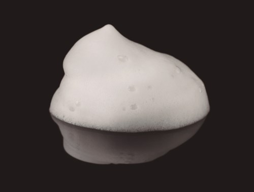 Soft, white foam with bubbles on a reflective surface, set against a black background.