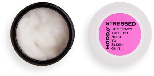 Ett litet runt behållare med vit kräm inuti och en rosa etikett som säger stresslindring och humör lugnande.