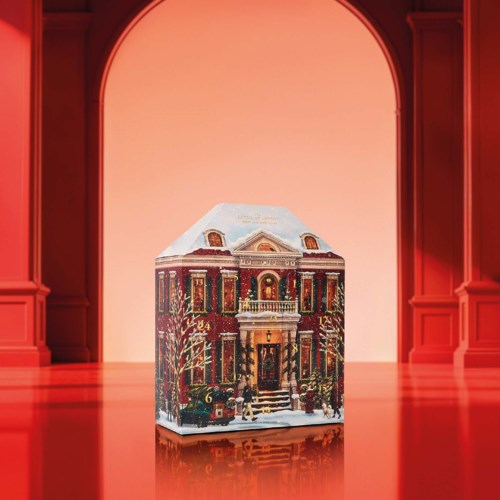 A festive, gingerbread house decorated with candies and icing, set inside a warm, elegant room with red walls and arch.