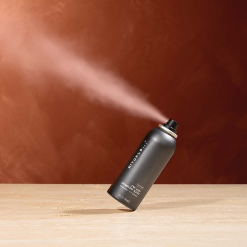 A black spray can releasing a fine mist of mist on a wooden surface with a brown background.