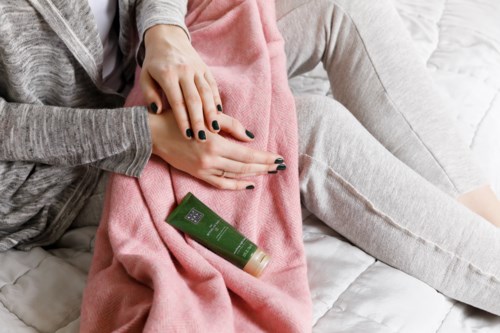 Personer sitter på en säng med ett rosa filttäcke och grå kläder. En grön lotionflaska finns på filten.