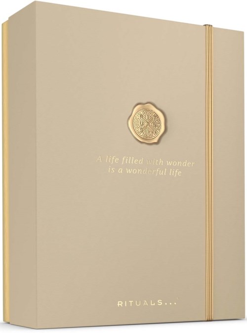 Een beige notitieboek met een goudkleurig embleem en inscriptie, voorzien van een bijpassend goudkleurig elastiek.