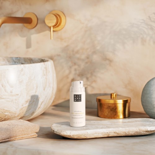 A white bottle labeled "OAK" on a marble tray, with gold and ceramic containers nearby, in a bathroom setting.