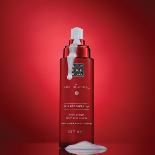 Red bottle of skin regeneration body serum with white foam on top and at the base, against a red background.