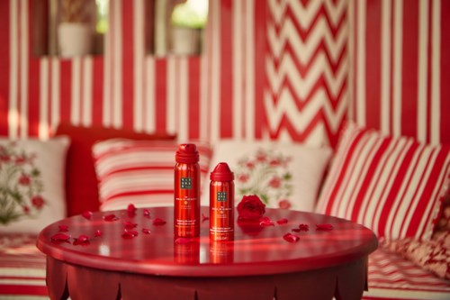 Two red bottles on a red table surrounded by red and white cushions and roses in a room with red striped walls.