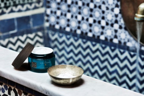 A jar of cream and a small bowl on a white marble ledge, with a patterned blue tile wall behind.