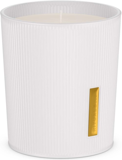 A white candle in a textured white holder with a small gold decorative element.