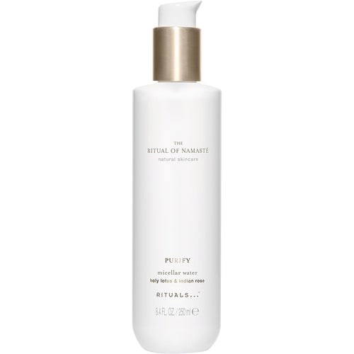 Een lange witte fles met een gouden dop, gelabeld als Purify micellaire water met lotusbloem en Indiase roos.