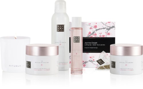 Skönhetsprodukter med vit och rosa förpackning, inklusive krämer, spray och en låda, arrangerade prydligt.