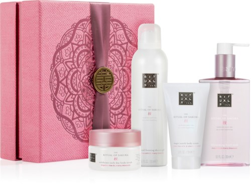 Pink box med dekorativt mönster och band, samt fyra hudvårdsprodukter i vita och rosa flaskor och krukor.