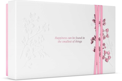 En hvid æske med pink detaljer og et citat: "Lykke kan findes i de mindste ting."