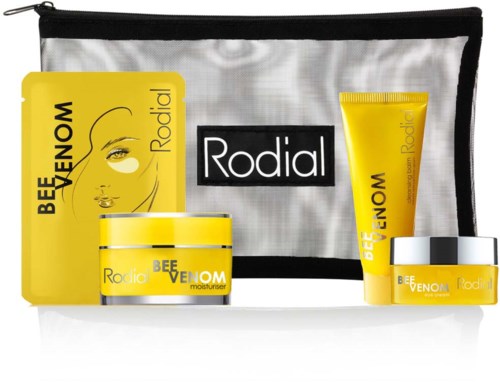 Produkty do pielęgnacji skóry w żółtym i białym opakowaniu, w tym kremy i żel, z torbą podróżną w tle.