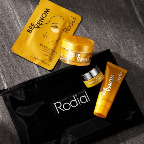 Produkty do pielęgnacji skóry obejmują maskę na twarz, krem i mały słoiczek, wszystko w żółtym opakowaniu, z torbą podróżną Rodial.