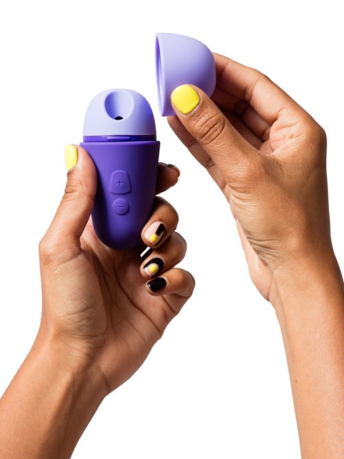 En person håller en liten lila enhet med lock, som visar en gul knapp, möjligen en massageapparat eller liknande.