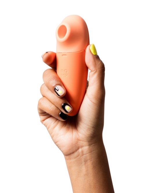 En hand håller en liten, orange enhet med rund top och ett hål, som liknar en massageapparat eller gadget.