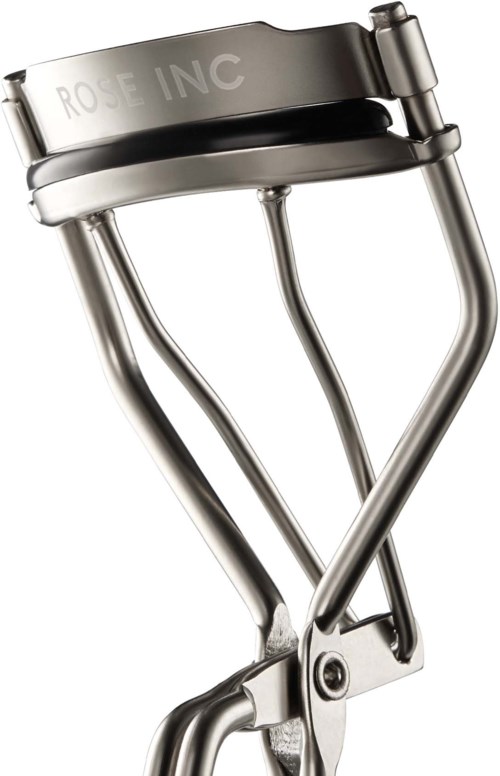 A metal eyelash curler with a black handle and silver metal parts, labeled 'ROSE INC' at the top.