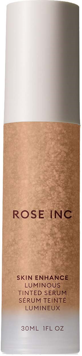 En lång, cylindrisk hudvårdsflaska med vit kork och beige kropp märkt 'ROSE INC' och 'Skin Enhance Luminous Tinted Serum.'