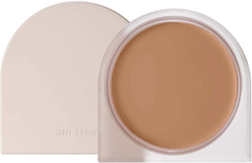 En krukke med beige foundation med hvit lokk, delvis åpen, som viser det kremaktige produktet inni.