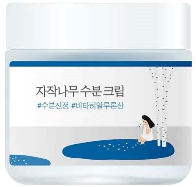 En hvid beholder med blå kanter viser en pige, der sidder ved vand, med koreansk tekst om en creme og hashtags.