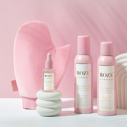 Rosa hudpleieprodukter med hvite lokk og en rosa klut, plassert på en hvit overflate med rosa bakgrunn.