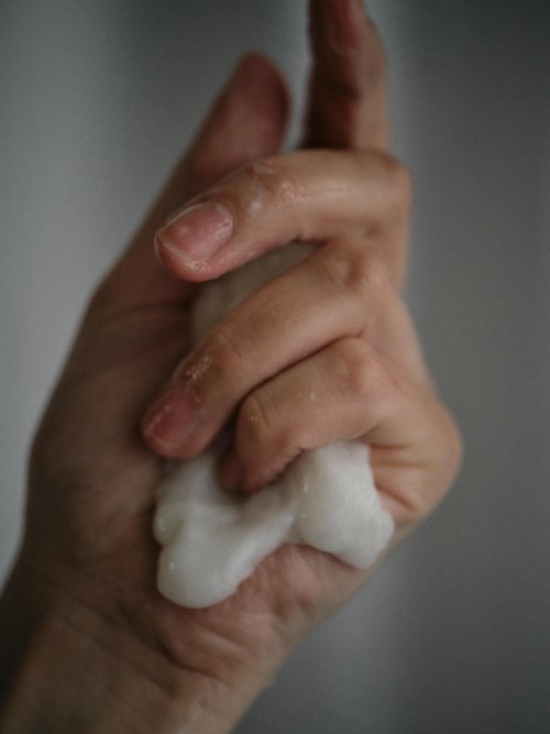 En hand som pressar ut ett mjukt, vitt ämne, möjligen tvål eller skum, mot en enkel bakgrund.