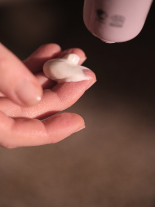 Dłoń nakłada lotion lub krem z butelki na palce w zbliżeniu.