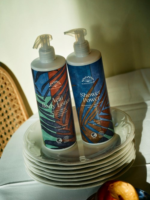 Two bottles of body lotion and shower power placed on a stack of plates. Some food is seen at the bottom.
