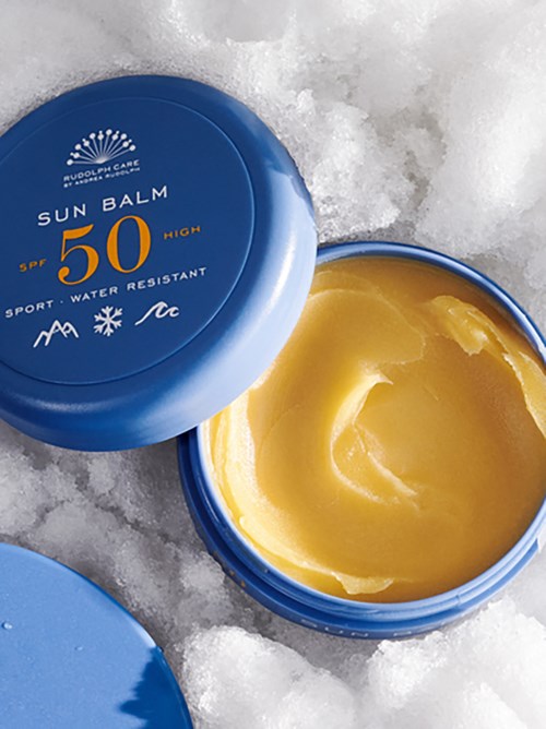 En blå burk av solkräm med SPF 50 är öppen på snö, som visar gul kräm inuti.